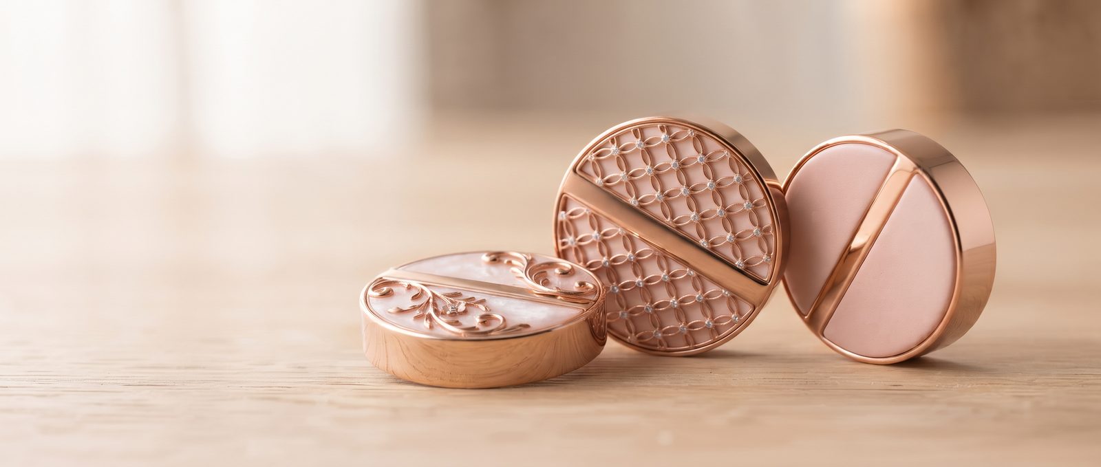 The three Juni Charm faces, Lace, Cut and Bare, in rose gold on a light oak table